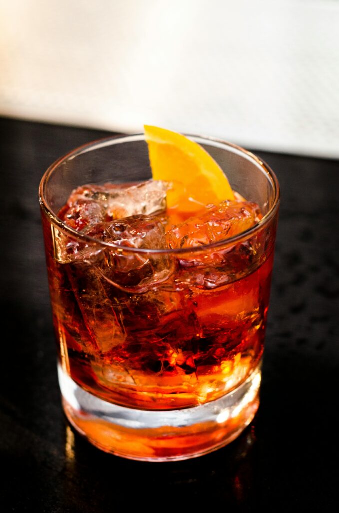 Chilled cocktail with orange slice garnish in a glass on a dark surface.