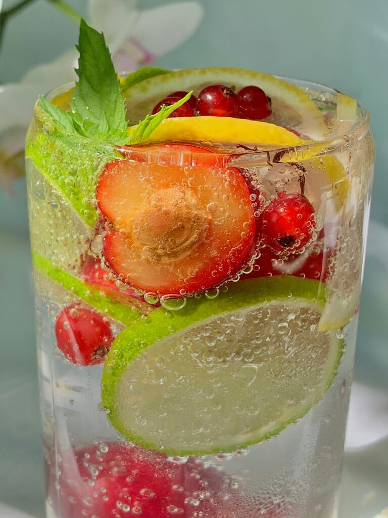 A vibrant glass of citrus and berry infused sparkling water with fresh mint leaves, offering a refreshing and healthy drink option.